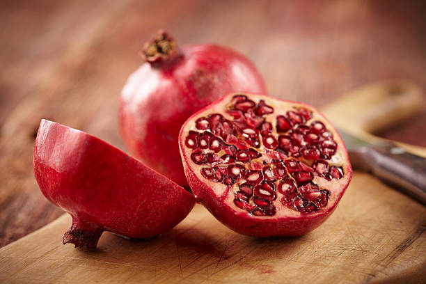 Pomegranate fruit on cut board Sliced pomegranate on cutting board with knife and whole pomegranate behind.  Shot with shallow focus on sliced fruit. pomegranate stock pictures, royalty-free photos & images
