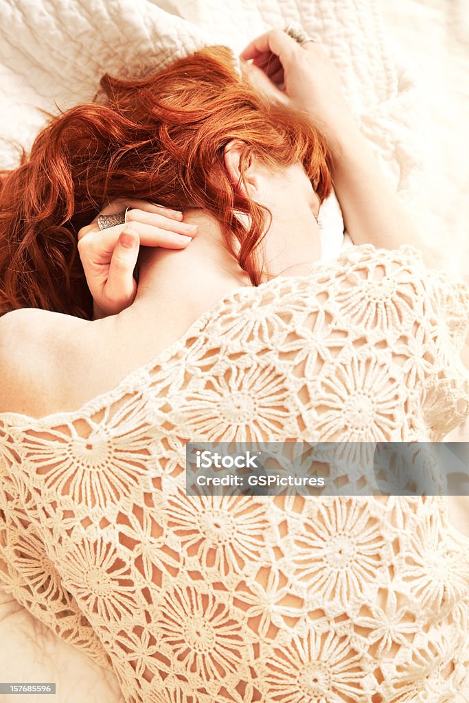 Redhead woman lying in bed with face obscured Overhead view of redhead woman lying in bed relaxing playing with her hair.  Face is obscured. Women Stock Photo