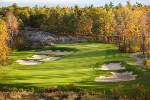 A beautiful golf course in the Muskoka region of Ontario, Canada in the fall. Golf courses in fall, with a myriad of colours, are often the prettiest. The pristine golf course, which has wonderful bunkering, is in immaculate condition. Turf grass maintenance standards are exceptional on this golf resort. Yellow aspens and maples highlight the surroundings with the boreal forest and Canadian Shield also highlights of the stunning golf facility. Nobody is in the image. 