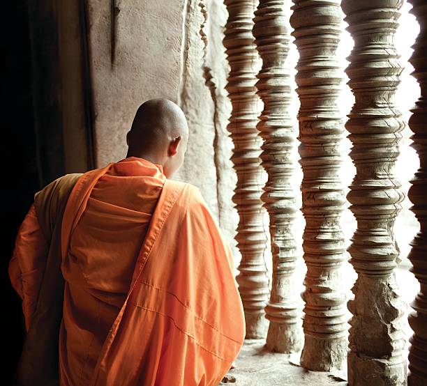 A monk wearing orange garments standing by pillars stock photo