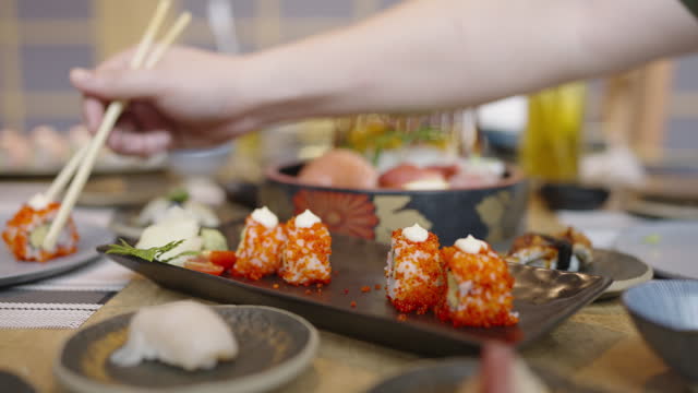 Side view, medium shot of a friend handing a California maki roll to their friends and taking one for them self during at Japanese restaurant
