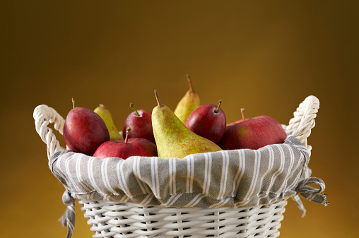 Close-up of fresh autumn fruits in white wicker basket on dark golden background.