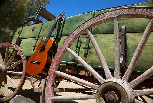 Classical guitar leaning against an old west wagon wheel from a covered wagon in desert setting