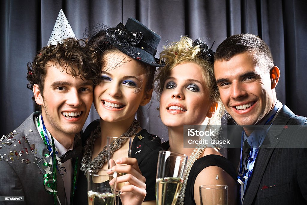 Happy New Year! Portrait of a well dressed young people celebrating New Year's Eve. They standing against grey curtain, toasting with champagne glasses, looking at camera and smiling.  Adult Stock Photo