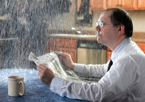 A man reads the paper as a bad roof leak allows rain down on him.