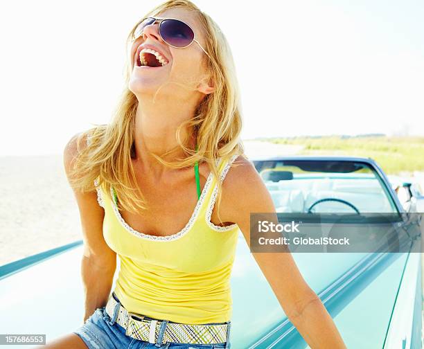 Foto de Jovem Mulher Usando Óculos De Sol Sentado No Carro Bonnet e mais fotos de stock de Camiseta sem Manga