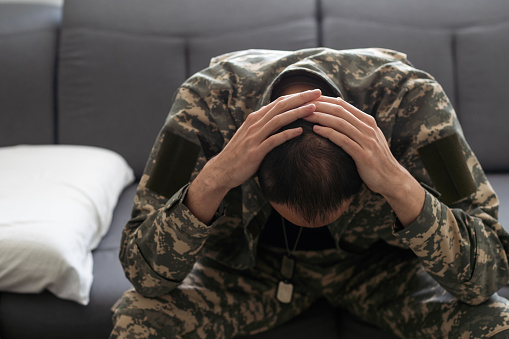 Having flashbacks. Post traumatic stress disorder. Soldier in uniform sitting indoors. High quality photo