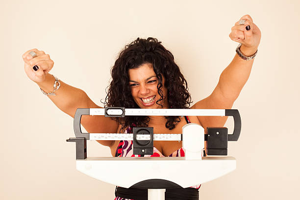 Celebrating weight loss Woman celebrating weight loss on a medical weight scale. dieting stock pictures, royalty-free photos & images