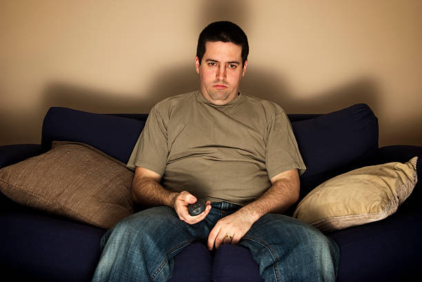 Bored, lazy, overweight man sits on the sofa  couch potato photos stock pictures, royalty-free photos & images