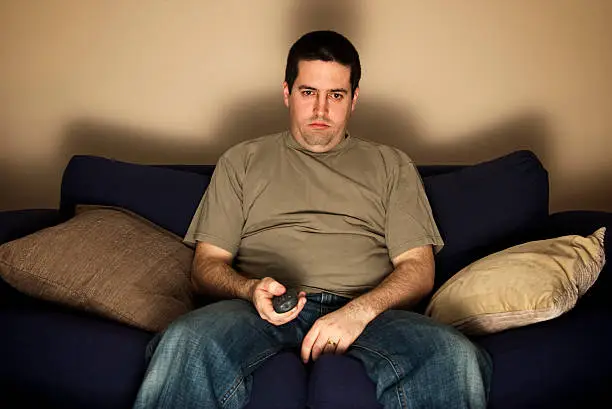Photo of Bored, lazy, overweight man sits on the sofa