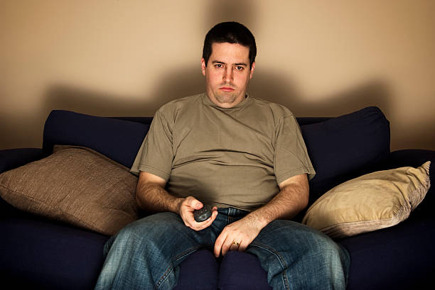 bored, lazy, overweight man sits on the sofa - 無聊 個照片及圖片檔