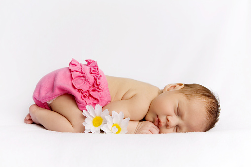 Newborn baby girl wearing pink diaper cover, asleep on her tummy with two daisies