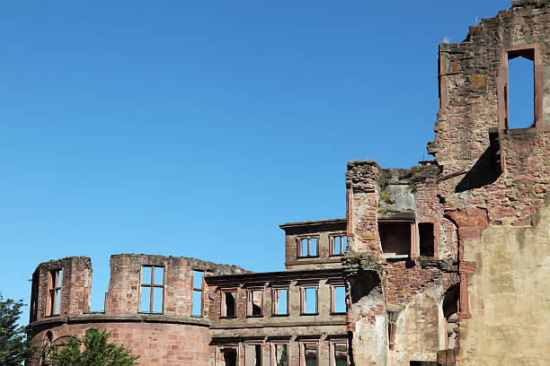 Weathered castle tower stands amidst vibrant greenery, showcasing historical architecture under bright sunlight in Heidelberg, Germany.