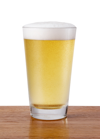 A refreshing pint of cold beer on a wood surface with white background.