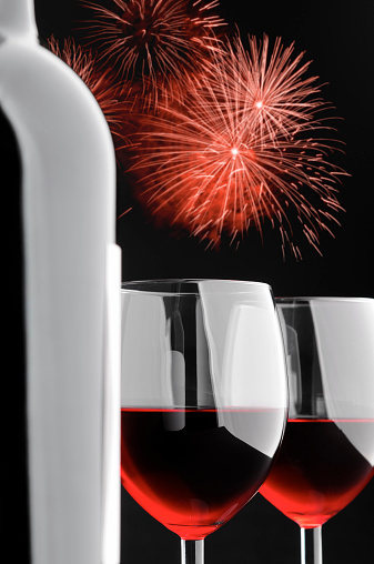 Close-up of two glasses of red wine and single wine bottle, against red fireworks on black background. Studio shot.