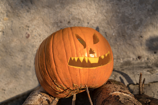 a pumpkin jack-o-lantern for Halloween outdoors on a stack of woods.