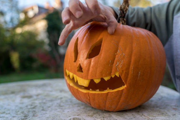 Childs' hand carving a pumpkin jack-o-lantern for Halloween outdoors on a table.