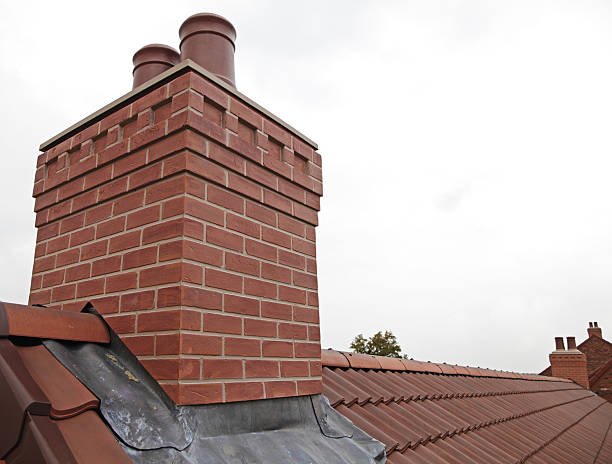 Brick chimney with two chutes sitting atop shingled roof stock photo