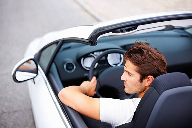 High angle of handsome young male driving convertible in speed  looking in mirror stock pictures, royalty-free photos & images