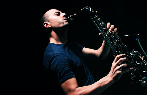 Male musician on stage plays the saxophone dark with smoke, copy space.