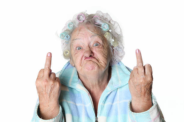 Senior Humor: cranky woman making faces and flipping the bird. 80ish senior female in rollers and plaid bathrobe is making faces. Humor image. cruel stock pictures, royalty-free photos & images