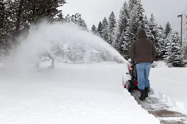 A man uses his snow blower to clear the driveway after a snowstorm.