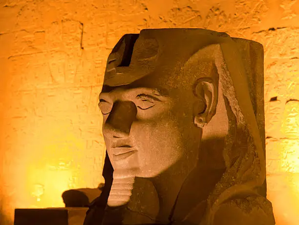 A huge granite statue of a pharoh lit up at night in luxor temple