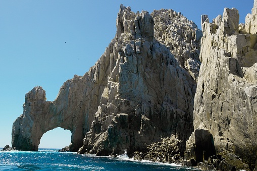 A scenic vista of two large rocks and two archways emerging from the calm water, with multiple boats sailing in the distance