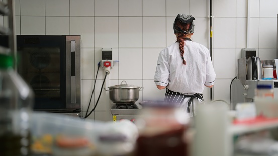 A young woman is working and cooking food in a commercial kitchen.