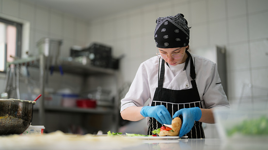 A young woman is working and preparing a sandwich in a commercial kitchen.