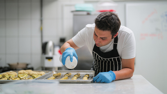A male chef is preparing baked food in a commercial kitchen.