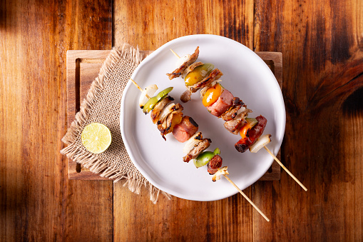 Homemade Skewers with meat and grilled vegetables served on a rustic wooden board, also known as brochettes, alambre, chuzo or pincho. Table topview.