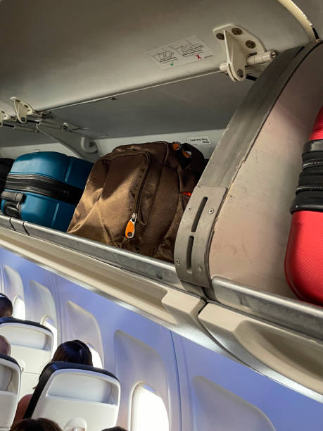 istock Full frame image of overhead baggage compartments with open doors in airplane cabin, row of suitcases, rucksacks and carryon luggage, focus on foreground 1577117322