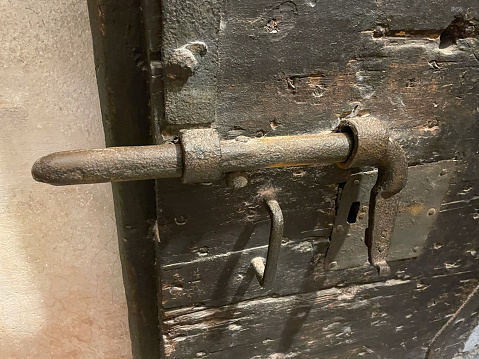 Stock photo showing close-up view of security mechanism of rusty metal door bolt on aged, heavy wood door.