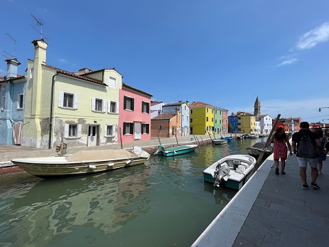 Burano, Venice, Italy - July, 13 2023: Stock photo showing view of tourists milling around a canal lined with colourful buildings and moored boats in Burano, Venice, Italy. Famous for lace making, Burano is an island in the Venetian Lagoon.