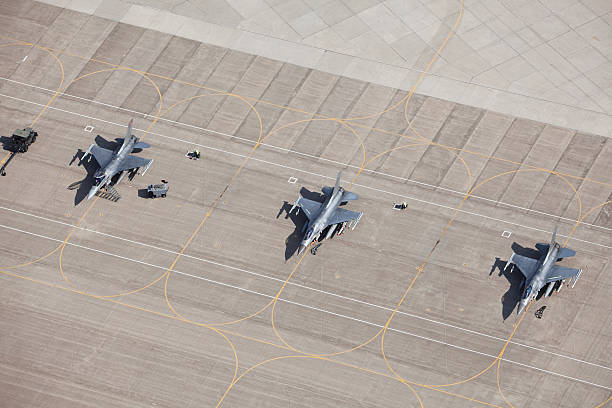 Three F-16 Fighter Jets on Tarmac Ready for Flight An aerial view of three F-16 fighter jets sitting on an airfield tarmac ready for flight. All have wing mounted fuel tanks and AMRAMM wingtip (air-to-air) missiles, the left two have Harm (air-to-ground) missiles. The left plane's canopy is open and the safety flags are removed for flight. The left two planes have safety flags in place. Shot from the open window of a small airplane.  http://www.banksphotos.com/LightboxBanners/Aerial.jpg http://www.banksphotos.com/LightboxBanners/Aircraft.jpg sidewinder missile stock pictures, royalty-free photos & images
