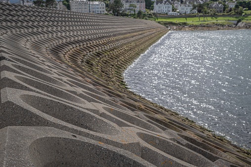 Bangor, County Down - July 15, 2023: Engineered rock armour protecting the breakwater of Bangor's marina and port.  Lining the coastline are Edwardian villas of Bangor West.