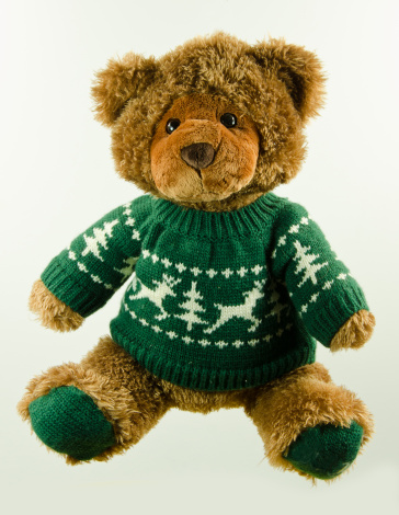 A teddy bear wearing a sweater on a white background. The Teddy has been used for years and shows loving wear.