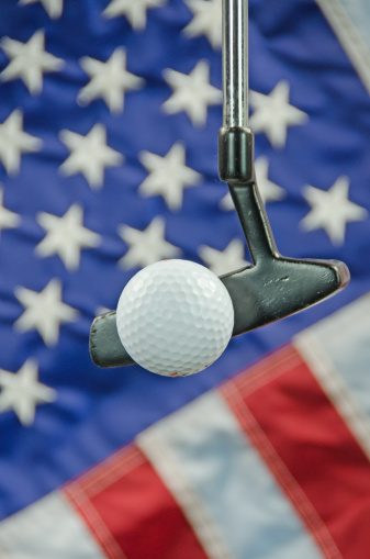 A golf ball and putter with a United States flag in the background.