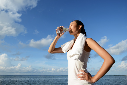 A young woman is drinking water after fitness with seascape background