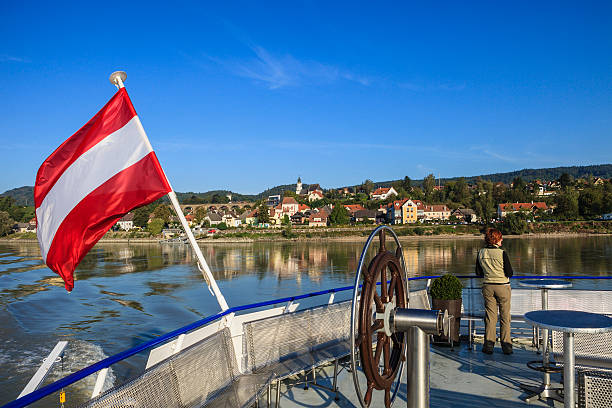 A woman is participating in a cruise along the Danube river in the Wachau, a region in the Lower Austria well-known for its wine growing area. It is about 40 kilometers (25 mi) in length and is located midway between the towns of Melk and Krems. It is inscribed in the UNESCO List of World Heritage Sites since December 2000.