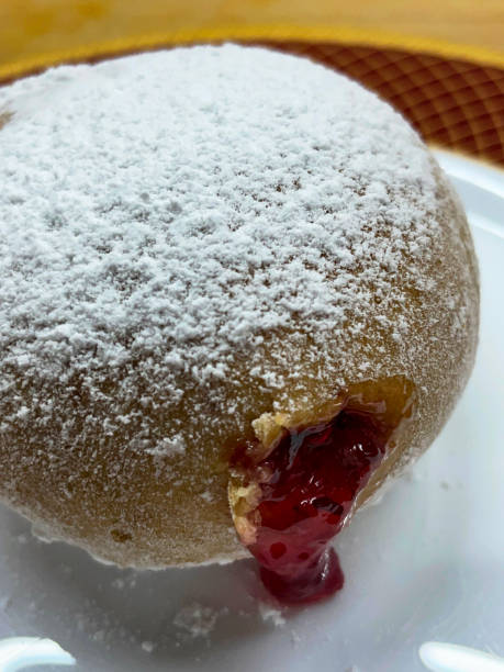 istock Close-up image of fresh jam doughnut coated in icing sugar on red rimmed plate, raspberry jam oozing onto plate, elevated view, focus on foreground 1577185365