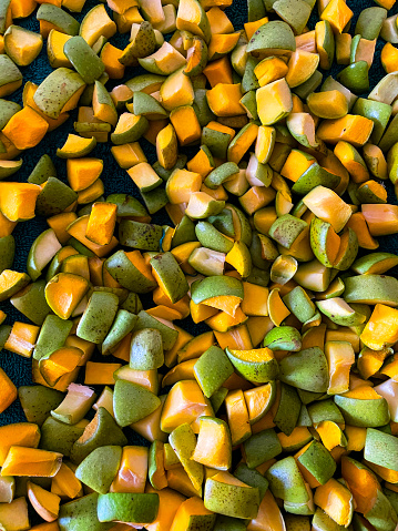 Stock photo showing close-up, elevated view of pile of fresh, cubed, tropical raw mango fruit showing green skin and orange flesh.
