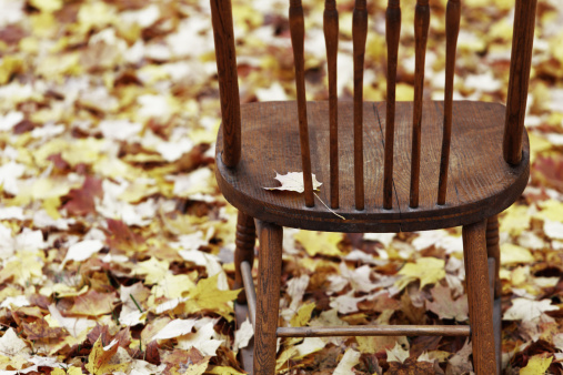 Low key, desaturated old antique rocking chair surrounded by a blanket of damp autumn leaves.