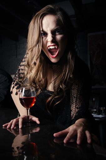 Portrait of a female vampire at the bar holding a glass of blood.
