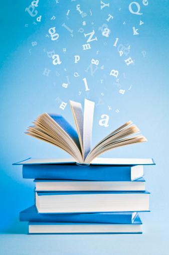 Stack of books, one book on the top is open, flying scattered letters in the background.