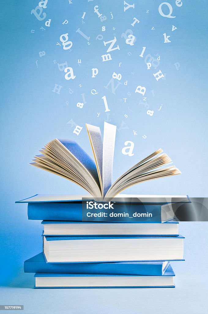 Open book with flying, scattered letters isolated on blue background Stack of books, one book on the top is open, flying scattered letters in the background. Book Stock Photo