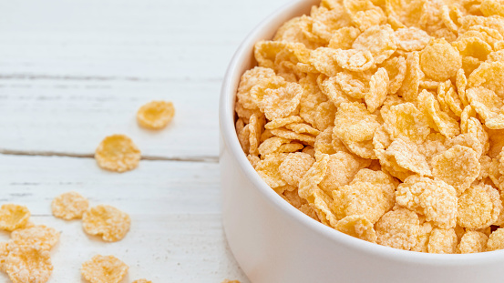 Ceramic bowl of corn flakes on white wood background with copy space. Traditional breakfast cereal.