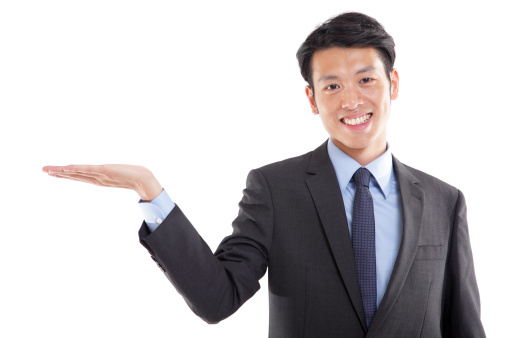 Young Asian businessman presenting something, looking at camera smiling, isolated on white background.