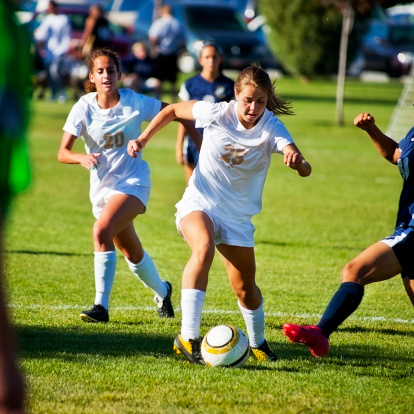 Attractive female soccer players converge on ball.